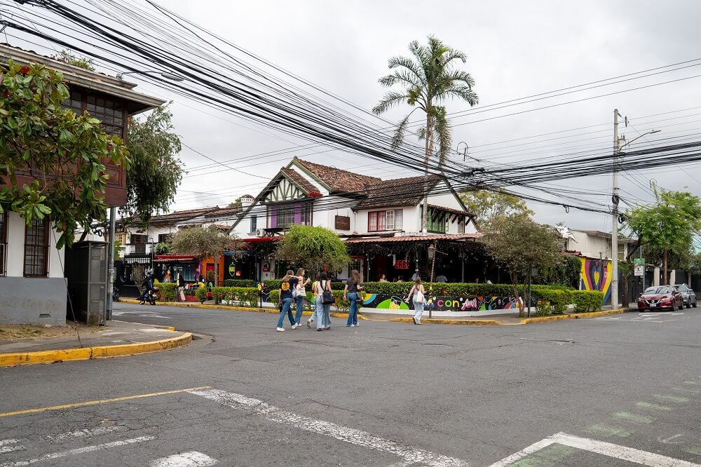 Pohled na městskou ulici s barevným café barem a lidmi přecházejícími křižovatku